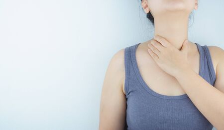 Closeup woman hand touching her neck suffering from sore throat. Health care and medical concept.の写真素材