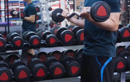 Young sporty man doing barbell curl in gym. Sport and exercise concept.