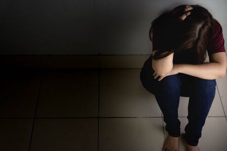 sad woman hug her knee and cry sitting alone in a dark room. Depression, unhappy, stressed and anxiety disorder conceptの写真素材