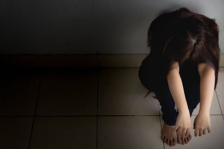 sad woman hug her knee and cry sitting alone in a dark room. Depression, unhappy, stressed and anxiety disorder conceptの写真素材