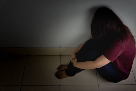 sad woman hug her knee and cry sitting alone in a dark room. Depression, unhappy, stressed and anxiety disorder conceptの写真素材