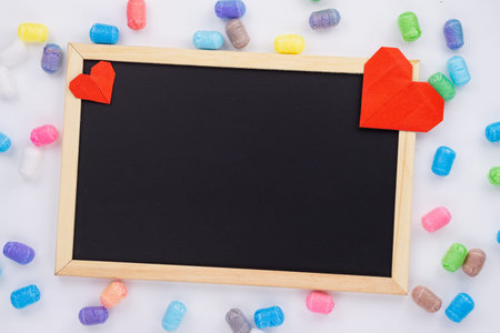 The red paper heart shapes and blackboard with colorful glitter over the white background. Greeting cards, Love and Valentines day concept. Flat lay, top view, copy space.の写真素材