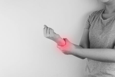 Black and white closeup woman holds her wrist pain with red spot. Health care and medical concept.の写真素材