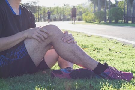 Knee Injuries. Young sport man holding knee with his hands in pain after suffering muscle injury during a running workout at park. Healthcare and sport concept.の写真素材
