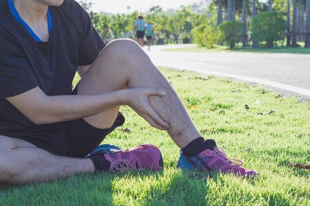 Young man massaging his painful calf ache from jogging and running outside at the park. Sport and exercise concept.の写真素材