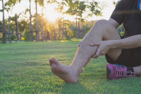 Young man massaging his painful calf ache from jogging and running outside at the park. Sport and...