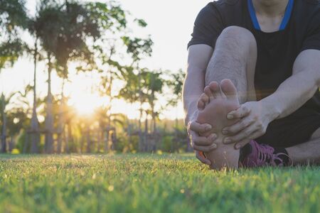 Young man massaging his painful foot from jogging and running on running track. Sport and exercise concept.の写真素材