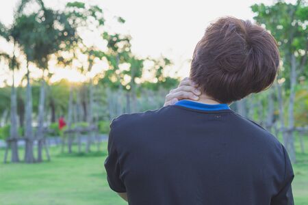 A male athlete suffering from neck and back pain and injury at the park. Sport and healthcare concept.の写真素材