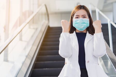 The business girl wearing mask for protecting coronavirus and pm 2.5 and show her hand to fight them while standing on the escalator. Coronavirus and Air pollution pm 2.5 concept.の写真素材