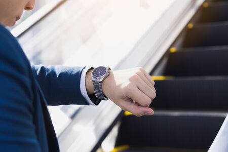 The photo close up of businessman watching his watch in his hand while standing on the escalator. Business and finance concept.の写真素材