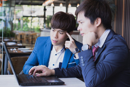 Business man thinking with caucasian colleague on common project while looking at laptop in the cafe shop.の写真素材