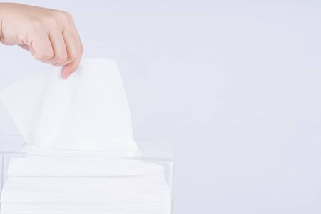 Delicate female hands pulling a white tissue paper out of a transparent crystal tissue box.の写真素材