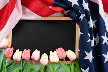 US American flag with blackboard and tulip flower on blue wooden background. For USA Memorial day, Presidents day, Veterans day, Labor day, Independence or 4th of July celebration. Top view, copy space for text.の写真素材