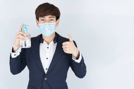 Asian handsome happy business man wearing a medical protection face mask for protect the coronavirus, filter dust PM 2.5 and cold and showing sanitizer hand gel and thumbs up on white backgroundの写真素材