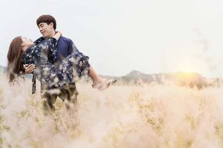 Summer portrait of young woman being carried by her boyfriend in meadow on sunny day. Couple having fun on their summer holiday.の写真素材