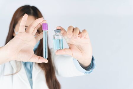 Closeup hand of woman doctor or scientist wearing medical mask and holding medicine liquid vaccine vial bottle. COVID 19 or coronavirus concept.の写真素材
