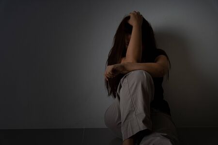 sad woman hug her knee and cry sitting alone in a dark room. Depression, unhappy, stressed and anxiety disorder concept.の写真素材