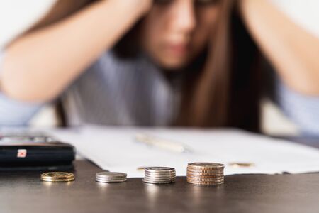 Close up coins on the desk with businesswoman working on desk office with depression, unhappy and stressed emotion. Expenses, taxes, home budget finance accounting concept.の写真素材