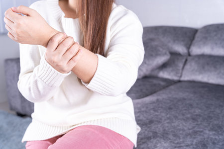 Young woman suffering from wrist pain while sitting on sofa at home. Healthcare medical or daily...