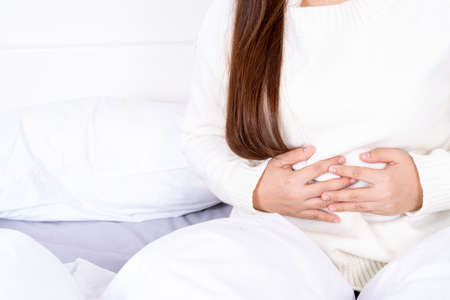 Young woman suffering stomach aches lying on the bed. Healthcare medical or daily life concept.の写真素材