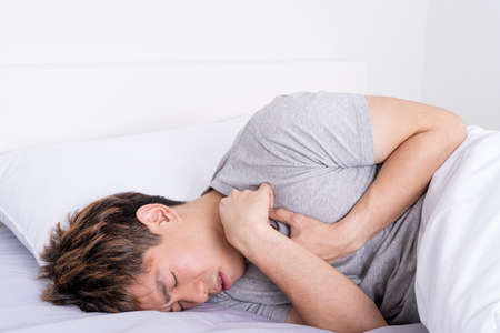 Young man suffering from chest pain after wake up on the bed. Healthcare medical or daily life concept.の写真素材