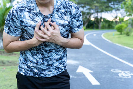 Exhausted male runner suffering painful angina pectoris or asthma breathing problems after running at the park. Sport and healthcare concept.の写真素材