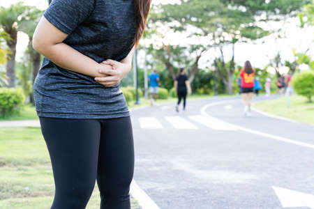 Asian woman suffering from stomach ache while running at the park. Injury from sport and exercise concept.の写真素材