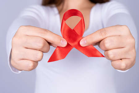 Red AIDS awareness ribbon holding by woman on grey background. World Aids Day, Healthcare and medical concept.の写真素材