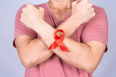 Red AIDS awareness ribbon on man arm and raise his hand to fight them on grey background. World Aids Day, Healthcare and medical concept.の写真素材