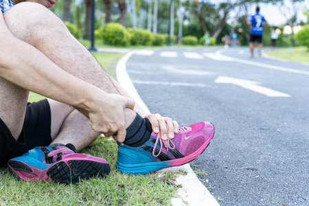Asian man use hands hold on his ankle while running on road in the park. Injury from workout...