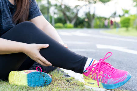 Asian woman massaging her painful calf ache from jogging and running outside at the park. Injury from sport and exercise concept.の写真素材