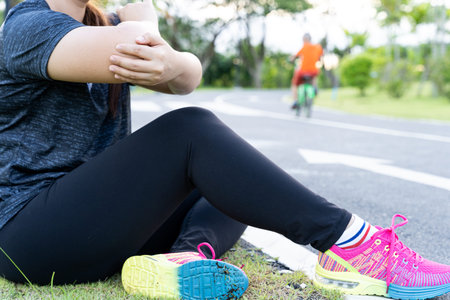 Asian woman suffering from arm and elbow pain from jogging and running outside at the park. Accident...
