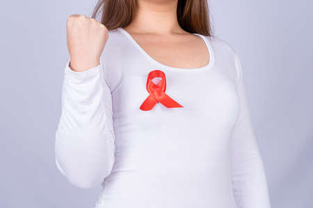 Red AIDS awareness ribbon on woman chest and raise her hand to fight them on grey background. World Aids Day, Healthcare and medical concept.の写真素材