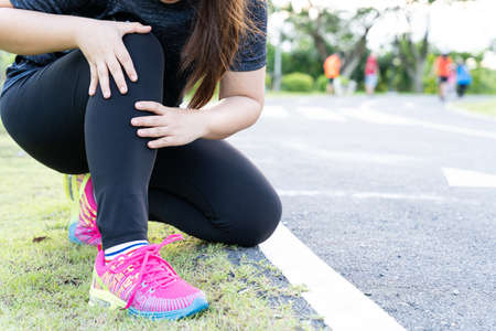 Asian woman use hands hold on her knee injury while running on road in the park, Injury from workout concept.の写真素材
