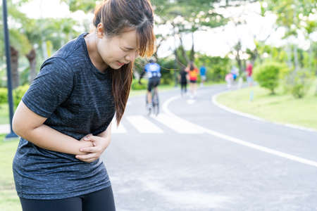 Asian woman suffering from stomach ache while running at the park. Injury from sport and exercise concept.の写真素材