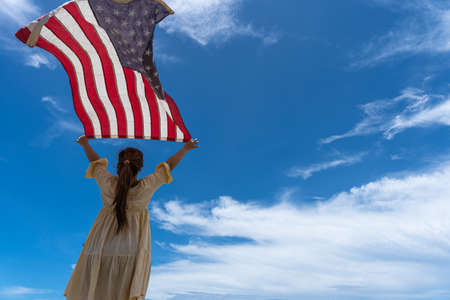 woman standing and holding USA flag under blue sky.の写真素材
