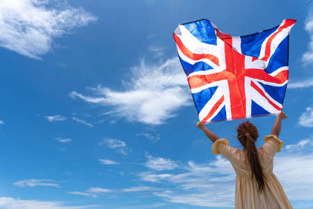 woman standing and holding UK flag under blue sky.の写真素材