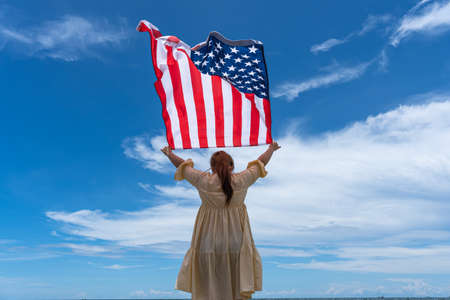 woman standing and holding USA flag under blue sky.の写真素材