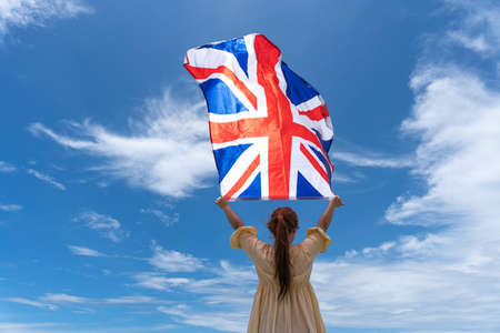 woman standing and holding UK flag under blue sky.の写真素材