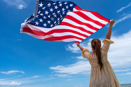 woman standing and holding USA flag under blue sky.の写真素材