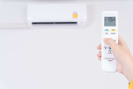 Human hand is using white remote of air conditioner for turn on or adjust temperature of air conditioner inside the room.の写真素材