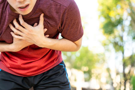 Exhausted male runner athlete suffering painful angina pectoris or asthma breathing problems while running in the park.の写真素材
