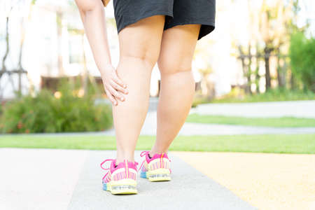 Female fatty runner athlete leg injury and pain. Hands grab painful leg while running in the park.の写真素材