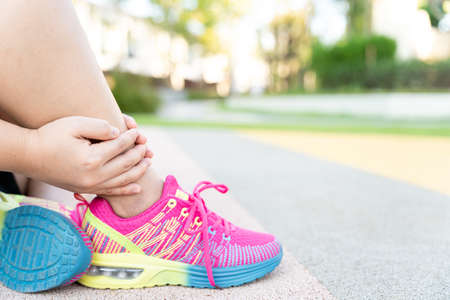 Female fatty runner athlete leg injury and pain. Hands grab painful leg while running in the park.の写真素材