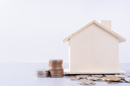 Wooden house with stack coins isolated grey background. Property investment and house mortgage financial concept.の写真素材