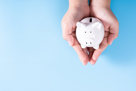 Hands hold a piggy bank isolated blue background. Saving money and investment concept.の写真素材