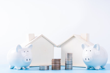 Piggy bank with wooden house and stack coins isolated grey background. Property investment and house mortgage financial concept.の写真素材