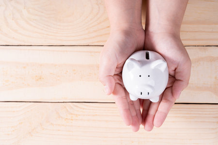 Hands hold a piggy bank on wooden background. Saving money and investment concept.の写真素材