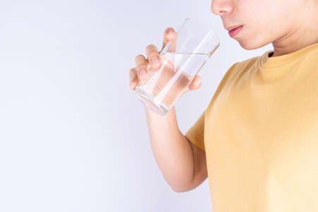 Man drinking water isolated grey background. Clean drinking water in clear glass.の写真素材
