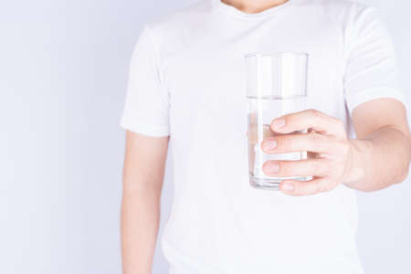 Man holding glass of water isolated grey background. Clean drinking water in clear glass.の写真素材
